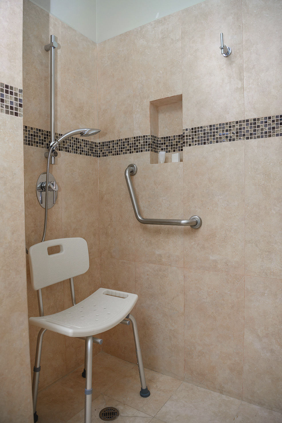 Baño moderno con diseño minimalista en tonos beige y blancos. Cuenta con una ducha a ras de suelo con mampara de cristal, un inodoro suspendido y un mueble de lavabo con cajones. Un armario empotrado de puertas blancas proporciona almacenamiento adicional, en un espacio bien iluminado y elegante.
